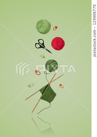 Tools for knitting warm clothes: scissors, green and red ball of thread, stoppers, and knitting needles with a knitted green piece of fabric flying in the air on a gray background. Hobby home crafts. Tools for knitting warm clothes: scissors, green and red ball of thread, stoppers, and knitting needles with a knitted green piece of fabric flying in the air on a gray background. Hobby home crafts. 129906778