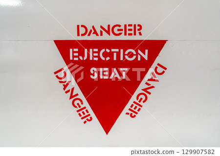 Ejection seat warning sign on an old aircraft fuselage close-up 129907582