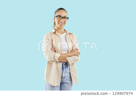 Confident girl on blue background stands with crossed arms, close-up 129907974