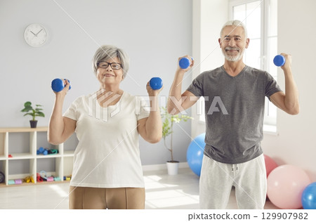 Happy Elderly Couple Exercising With Dumbbells In Gym Happy Elderly Couple Exercising With Dumbbells In Gym 129907982