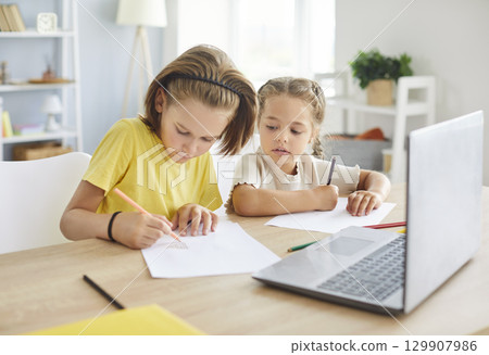 Two focused preteen children sitting together at table, drawing and enjoying creative activities. 129907986