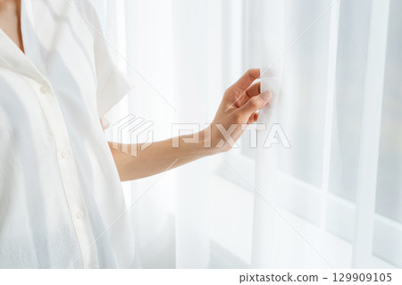 A woman standing by the window and opening the curtains 129909105
