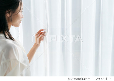 一位女士站在窗邊,拉開窗簾 一位女士站在窗邊,拉開窗簾 129909108