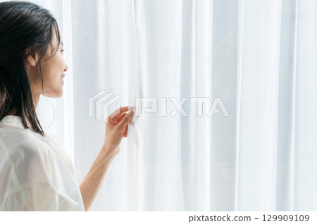 A woman standing by the window and opening the curtains A woman standing by the window and opening the curtains 129909109