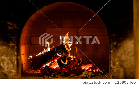 Cozy fireplace burning logs in a brick hearth during the evening hours creating a warm atmosphere for relaxation Cozy fireplace burning logs in a brick hearth during the evening hours creating a warm atmosphere for relaxation 129909460