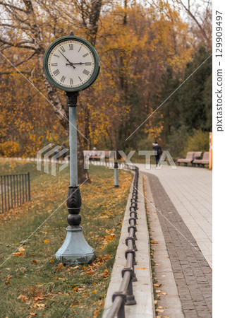Classic clock stands tall in park surrounded by autumn leaves on a quiet afternoon Classic clock stands tall in park surrounded by autumn leaves on a quiet afternoon 129909497