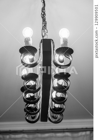 Elegant black and white chandelier with glowing bulbs hanging from the ceiling in a classic interior setting Elegant black and white chandelier with glowing bulbs hanging from the ceiling in a classic interior setting 129909501