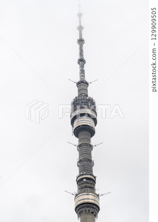 Cloudy day view of a tall communication tower rising above the skyline in a city location 129909505