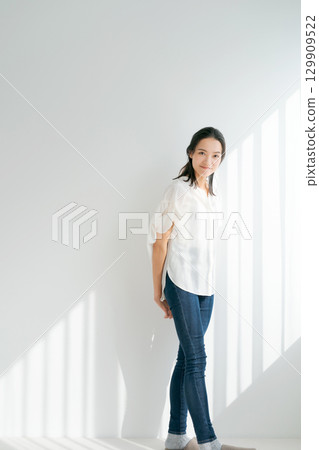 Woman in denim standing by the window (vertical) 129909522
