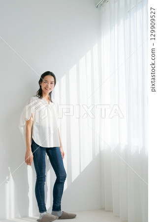 穿著牛仔布的女人站在窗邊(垂直) 穿著牛仔布的女人站在窗邊(垂直) 129909527