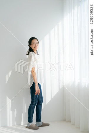 穿著牛仔布的女人站在窗邊（垂直） 129909528