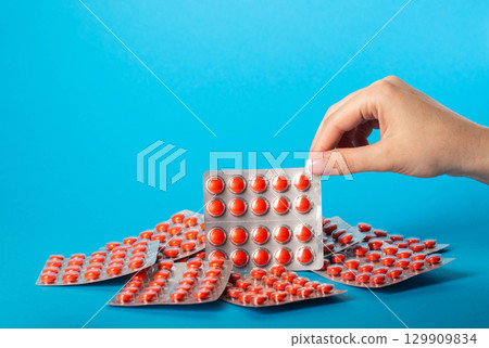 Female hand holding a blister pack with red pills on a blue background. Glycopeptide antibiotics concept. Copy space for text 129909834