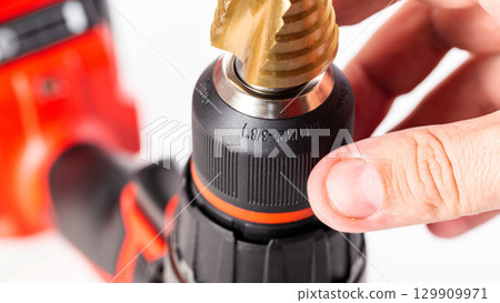 Modern red drill screwdriver with step drill bit in keyless chuck on white background, close-up 129909971