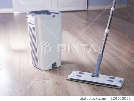 Modern mop with wringing bucket in room against room interior background. Apartment cleaning, close-up Modern mop with wringing bucket in room against room interior background. Apartment cleaning, close-up 129910031