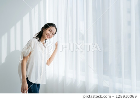 A woman in denim standing by the window 129910069