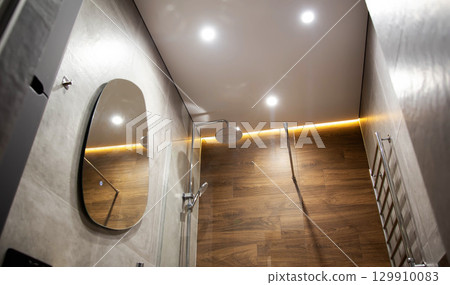 Modern bathroom with wood tiles, mirror and stretch ceiling with LED lighting. Chrome shower and heated towel rail, modern renovation Modern bathroom with wood tiles, mirror and stretch ceiling with LED lighting. Chrome shower and heated towel rail, modern renovation 129910083