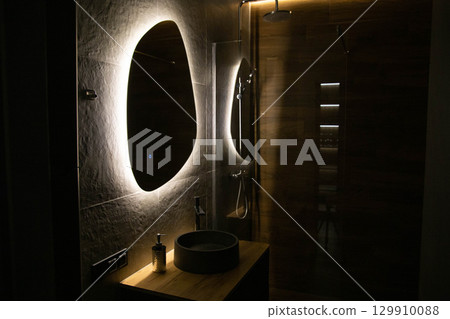 Fashionable interior in the shower with a mirror with diode backlighting and diode strip in the ceiling and wood-like tiles. Modern shower, copy space for text 129910088