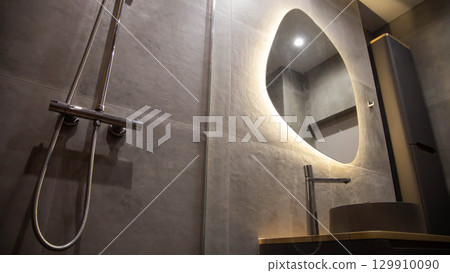 Stylish modern mirror with diode backlight against the background of a gray tiled wall in the bathroom, close-up 129910090