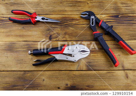 Set of different pliers on wooden background. Top view Set of different pliers on wooden background. Top view 129910154