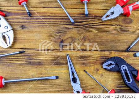 Set of different pliers and screwdrivers on wooden background. Top view, copy space 129910155