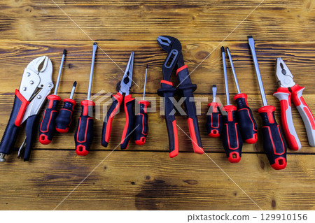 Set of different pliers and screwdrivers on wooden background. Top view Set of different pliers and screwdrivers on wooden background. Top view 129910156