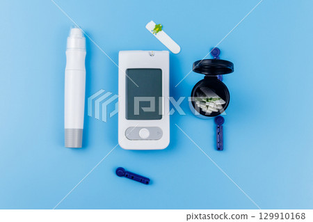 Digital glucometer, lancet pen, disposable needles and test strips on pastel blue background. Top view. Diabetes concept Digital glucometer, lancet pen, disposable needles and test strips on pastel blue background. Top view. Diabetes concept 129910168