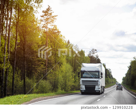 Truckers transport cargo on trucks in summer against the backdrop of forest and nature. Logistics company concept. GPS monitoring, transport company as a business. Copy space for text Truckers transport cargo on trucks in summer against the backdrop of forest and nature. Logistics company concept. GPS monitoring, transport company as a business. Copy space for text 129910228