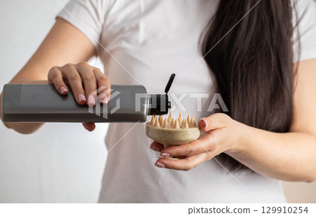 Girl pours shampoo on massager to massage and cleanse head, close-up. Hair care Girl pours shampoo on massager to massage and cleanse head, close-up. Hair care 129910254