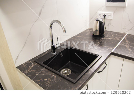 Black modern sink with water tap built into granite worktop in kitchen, industry Black modern sink with water tap built into granite worktop in kitchen, industry 129910262