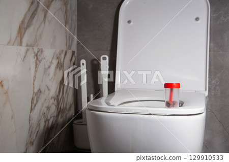 Sterile container with stool test on the toilet bowl in the toilet. Concept of stool examination for oviworm and coprogram. Copy space for text, biochemical 129910533