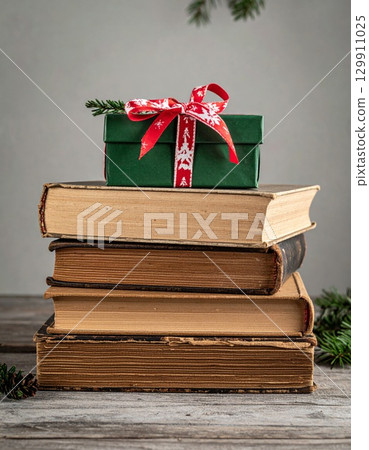 Vintage Book Stack with Green Christmas Gift Box and Red Ribbon on Wood Table 129911025