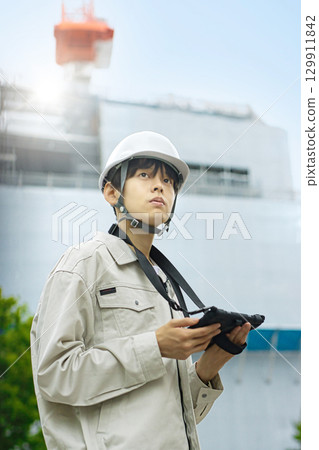穿著工作服的年輕商人在建築工地上看著平板電腦 穿著工作服的年輕商人在建築工地上看著平板電腦 129911842