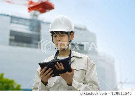 Young businessman in work clothes looking at a tablet at a construction site Young businessman in work clothes looking at a tablet at a construction site 129911843