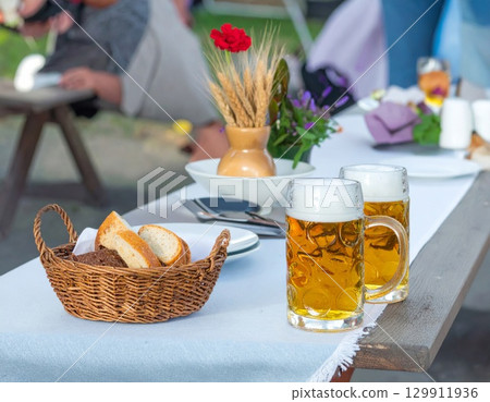 Golden Beer Glasses with Breads and Red Flower on a Table Outdoors Picnic Scene 129911936