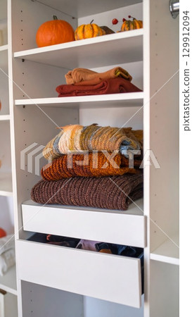 White Closet Shelf with Folded Knit Sweaters and Decorative Pumpkins Stacked Nicely 129912094