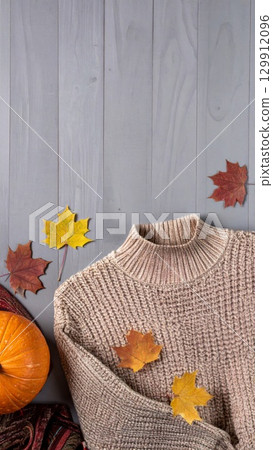 Cozy Brown Sweater with Pumpkin and Colorful Fall Leaves on a Gray Wooden Table 129912096