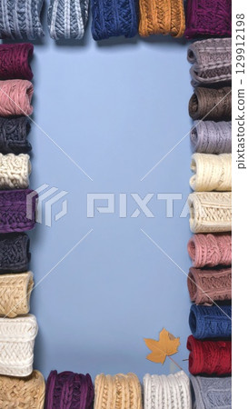 Colorful Knitted Scarves Border on Blue Background with Single Autumn Leaf 129912198