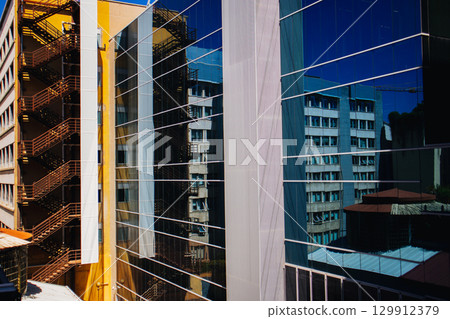 Modern building with glass facade reflecting surrounding structures and fire escape. Architectural shot Modern building with glass facade reflecting surrounding structures and fire escape. Architectural shot 129912379