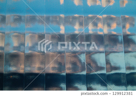 Reflective glass facade showcasing an abstract, geometric design and blue sky Architectural shot featuring reflecting blue sky in a glass facade 129912381
