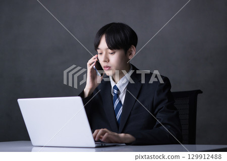 一位年輕的商人一邊看著電腦，一邊用智慧型手機聊天 129912488