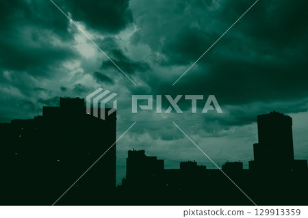 A dramatic cityscape at night features silhouettes of the buildings against moody sky with dark low clouds. Slhouetted district under overcast skyline A dramatic cityscape at night features silhouettes of the buildings against moody sky with dark low clouds. Slhouetted district under overcast skyline 129913359