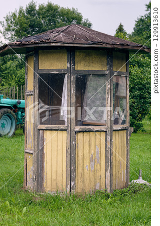 Old wooden shelter stands in a green field beside a tractor on a sunny day in a rural area 129913610