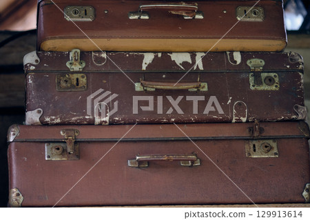 Vintage brown suitcases stacked in a rustic setting, showcasing wear and history of travel experiences and adventures 129913614