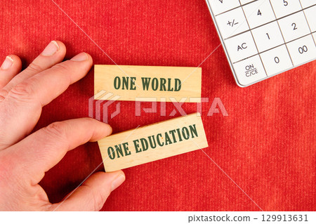 Education and knowledge concept. Copy space. ONE WORLD ONE EDUCATION assembled from blocks in a composition with part of a white calculator and a hand, top view 129913631