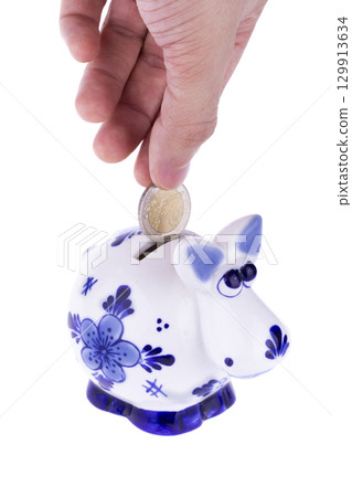 Piggy bank in a shape of a cow with blue ornament, coin falling Piggy bank in a shape of a cow with blue ornament, coin falling 129913634