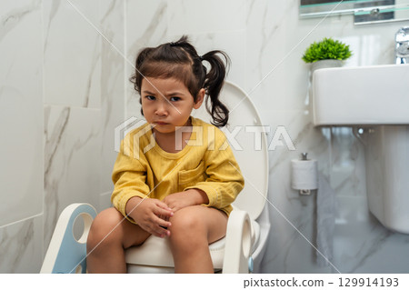 toddler girl sitting on toilet at home and suffering from stomachache and constipation toddler girl sitting on toilet at home and suffering from stomachache and constipation 129914193