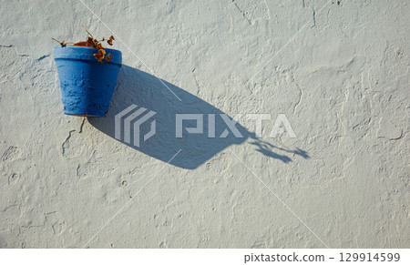 Blue flower pot on white wall with long shadow in Andalusian street Blue flower pot on white wall with long shadow in Andalusian street 129914599
