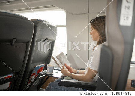 Reading a Book While Traveling on a Train in the Afternoon With a Cup of Coffee Beside Her 129914813