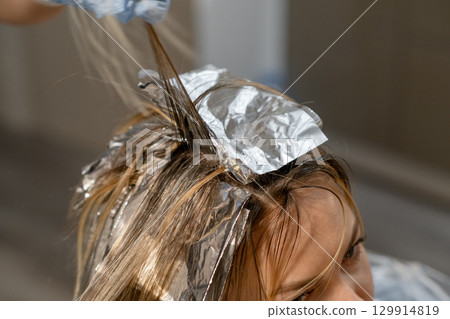 Hair coloring process in a salon with foils and a stylist focused on strand technique Hair coloring process in a salon with foils and a stylist focused on strand technique 129914819