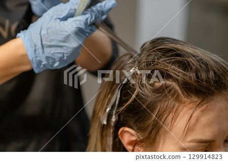 Hair coloring process in a salon with a stylist applying color to long hair during a bright afternoon session 129914823